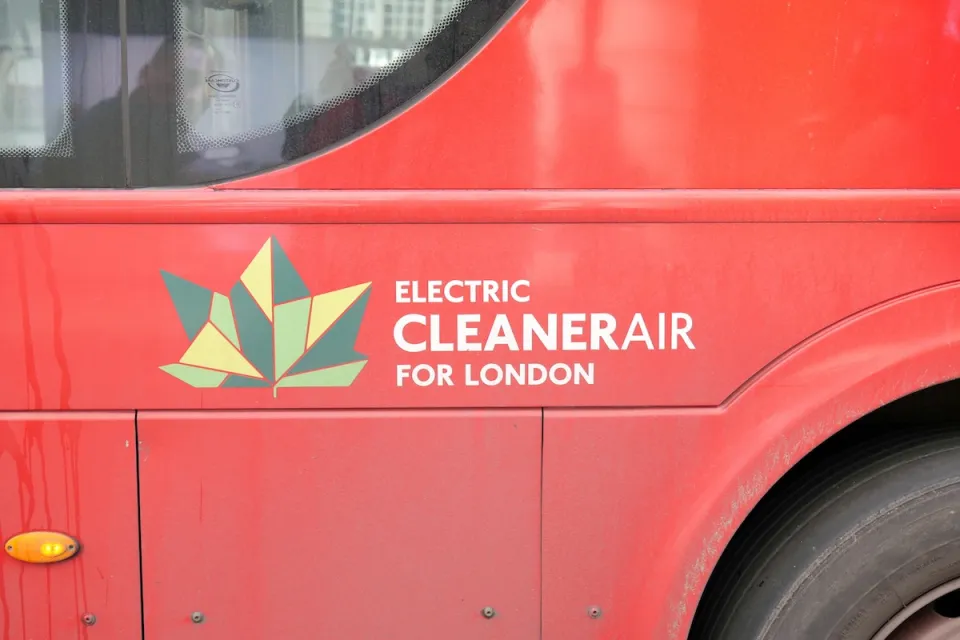 Close-up of geometric green leaf logo and "Electric Cleaner Air for London" white text on side of red London bus.